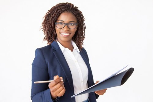 Happy successful business leader signing agreement, holding pen and documents, looking at camera. Young African American business woman posing isolated over white background. Signing contract concept